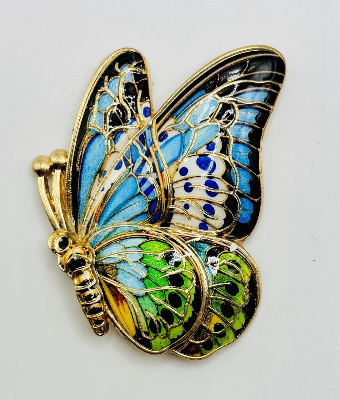 Blue, green, and gold enamel butterfly needle minder on a white background