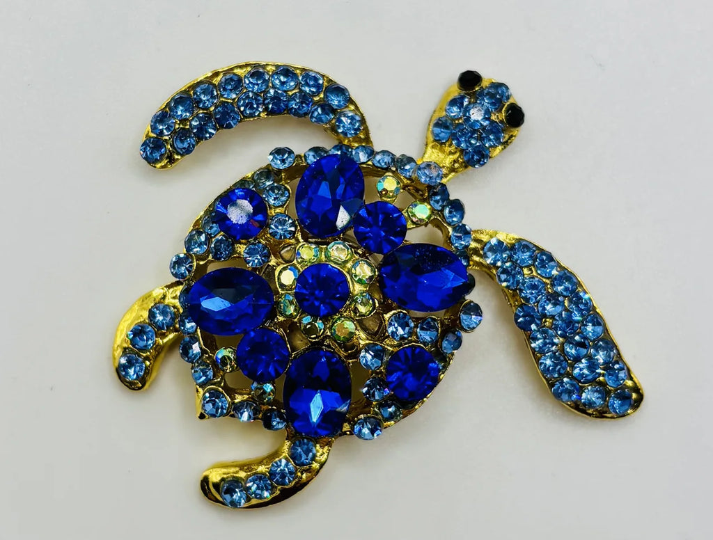 Blue, green, and gold enamel blue sea turtle needle minder on a white background