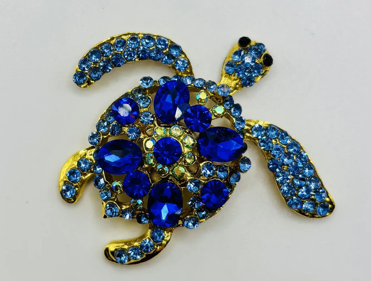 Blue, green, and gold enamel blue sea turtle needle minder on a white background
