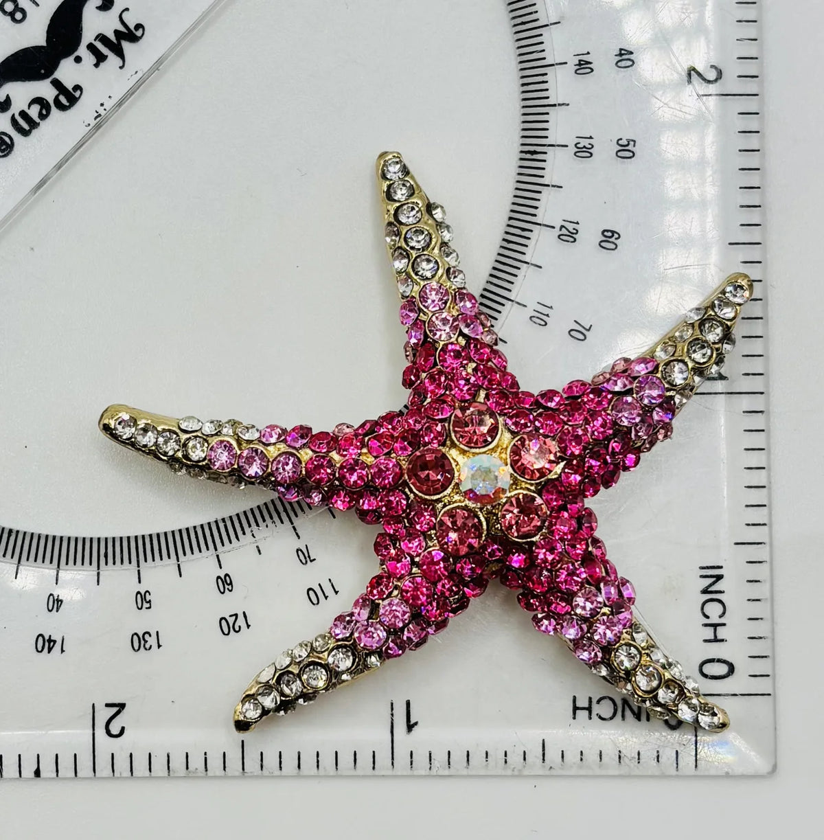 Pink crystal starfish needle minder beside a ruler for scale