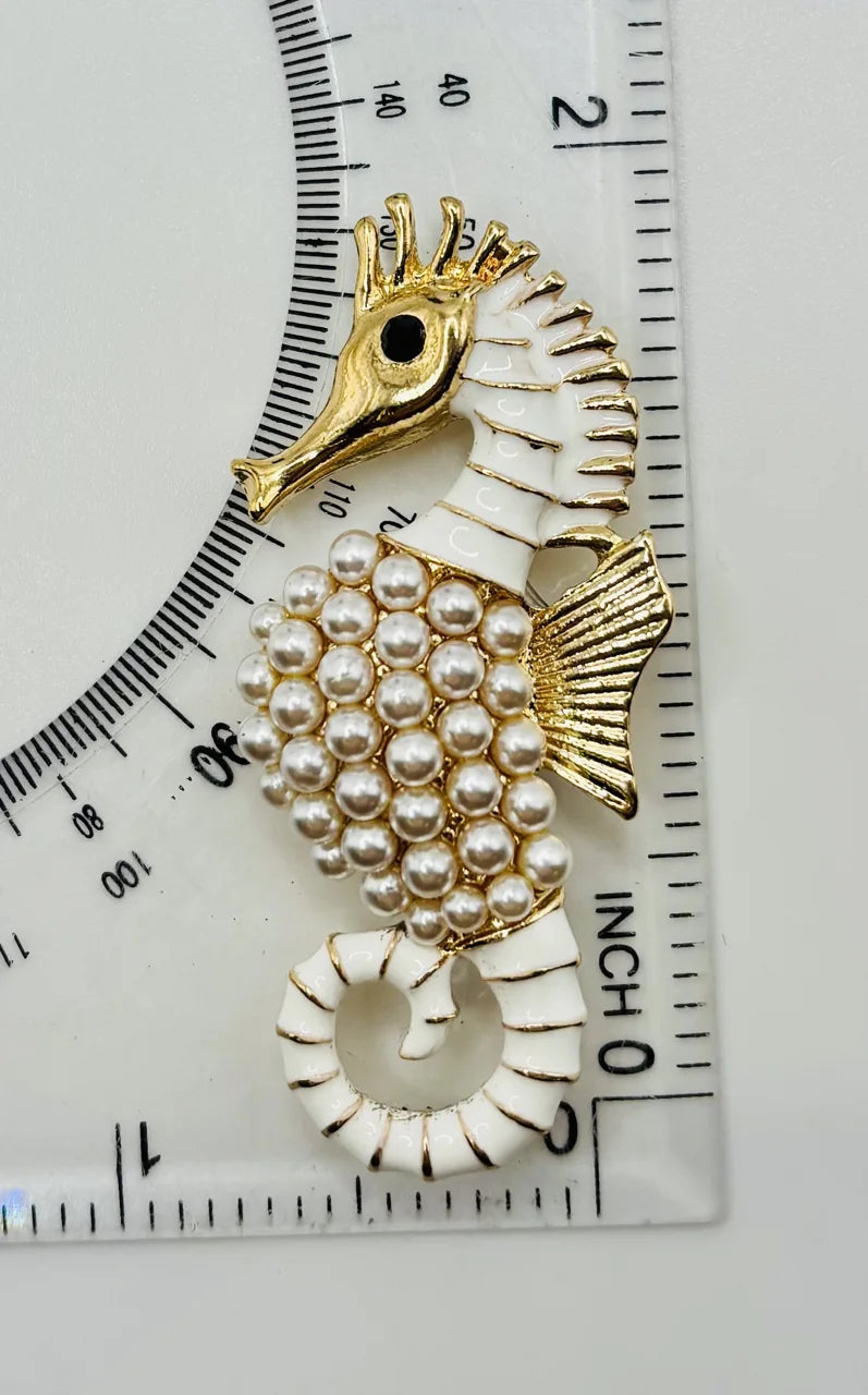 Gold and pearl seahorse needle minder beside a ruler for scale