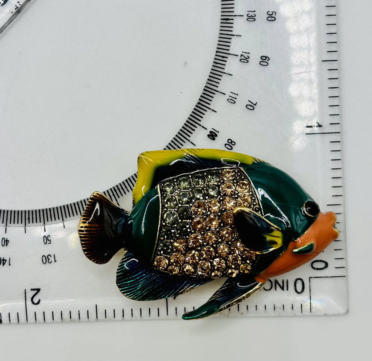 Colorful enamel and crystal tropical fish needle minder beside a ruler for scale