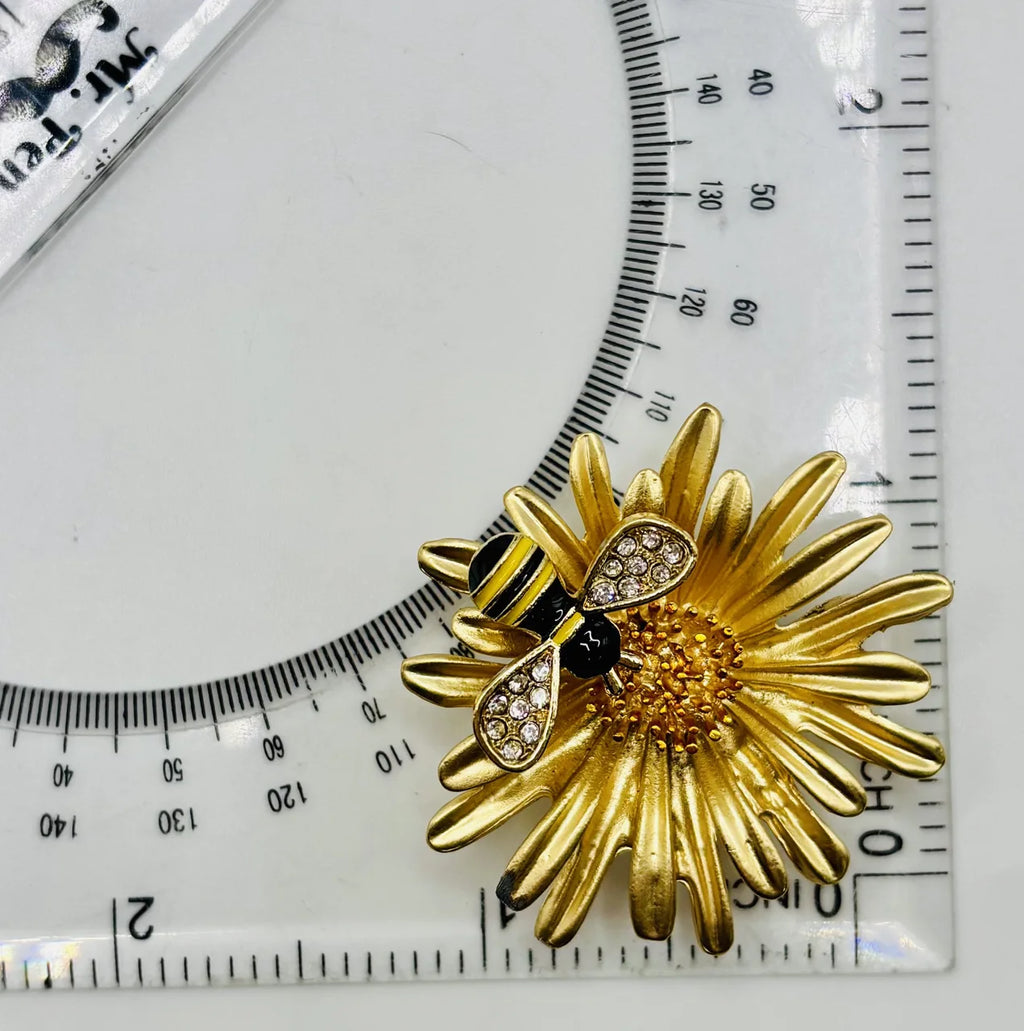 Enamel daisy with bee needle minder beside a ruler for scale