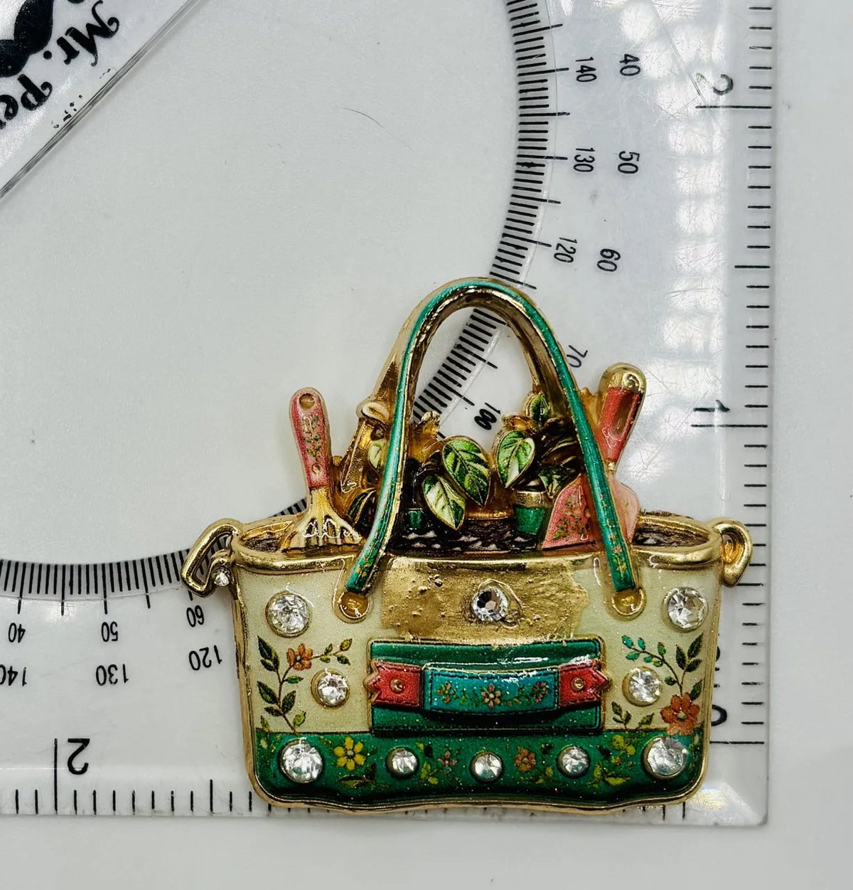 Enamel and crystal gardeners tote needle minder beside a ruler for scale