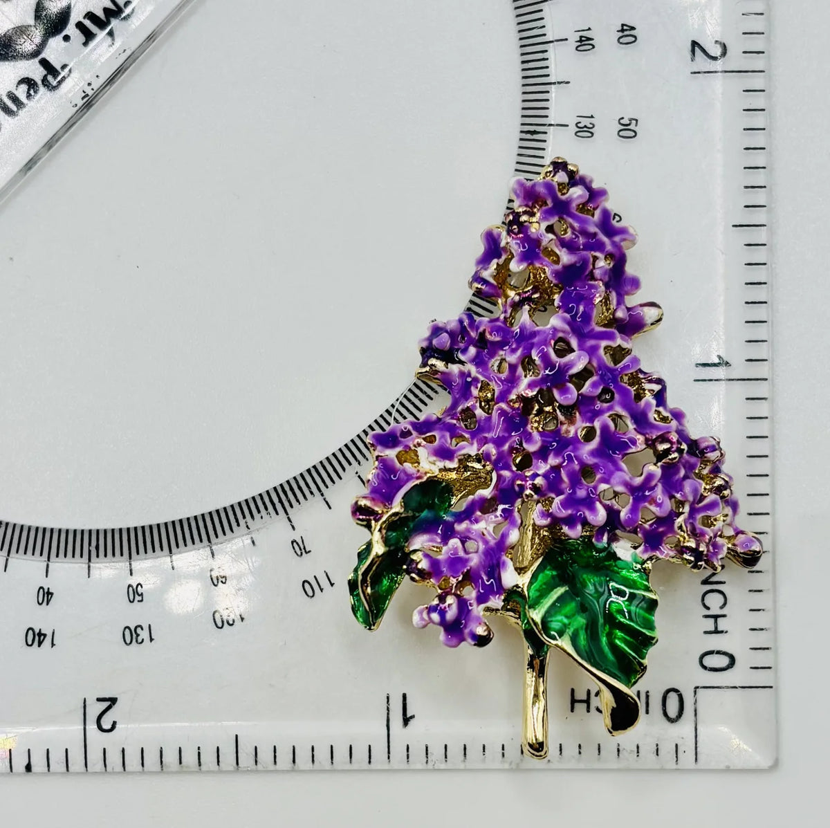 Enamel lavender lilac needle minder beside a ruler for scale