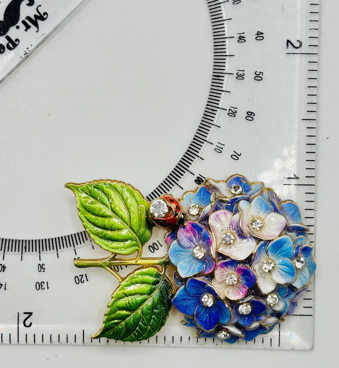 Blue and lavender hydrangea needle minder beside a ruler for scale