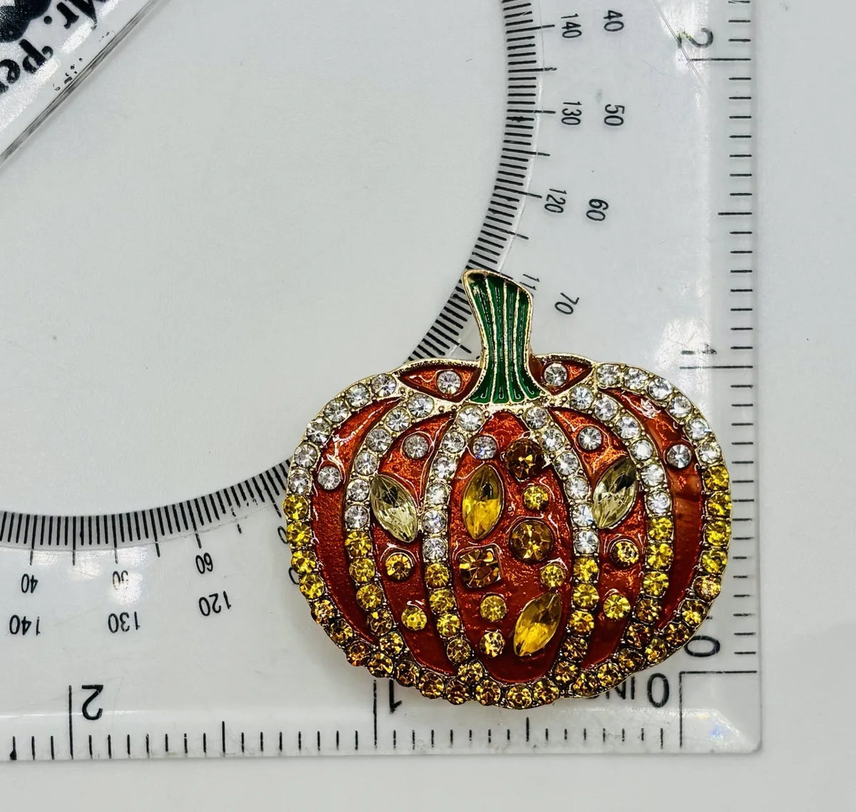 Orange enamel and crystal pumpkin needle minder beside a ruler for scale