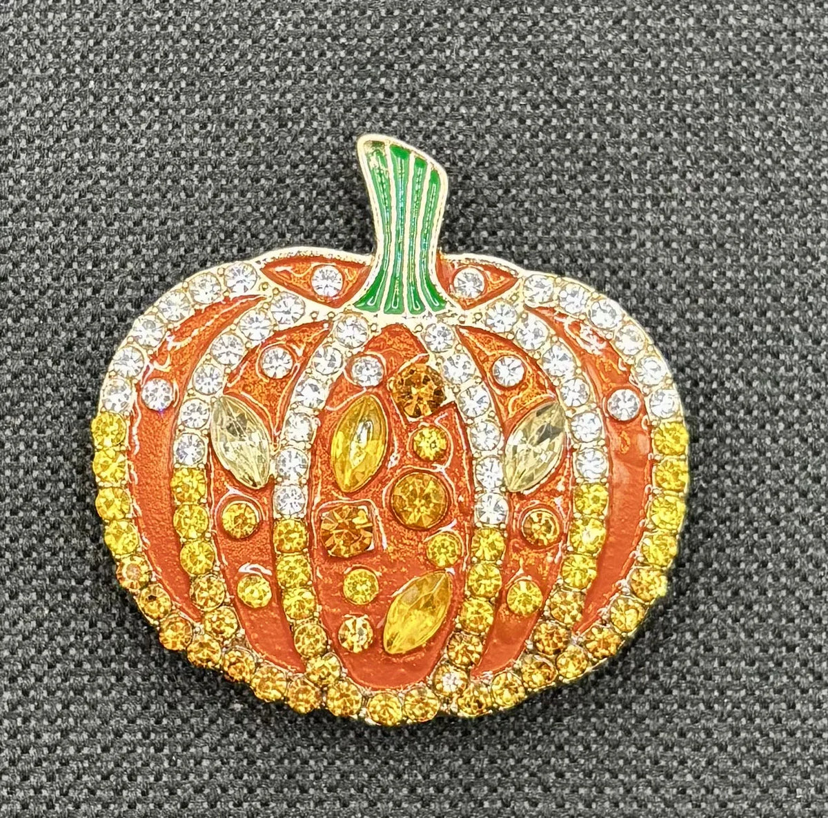 Orange enamel and crystal pumpkin needle minder on dark fabric