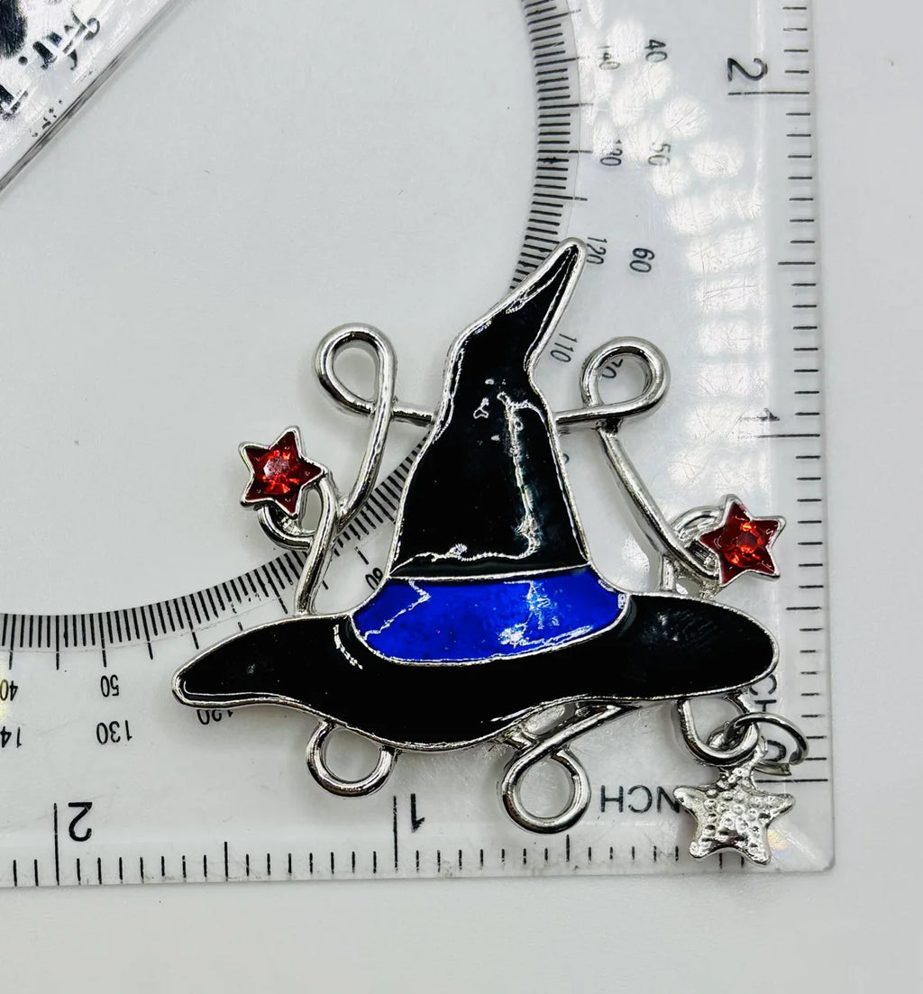 Enamel witch hat with dangling crystals needle minder beside a ruler for scale