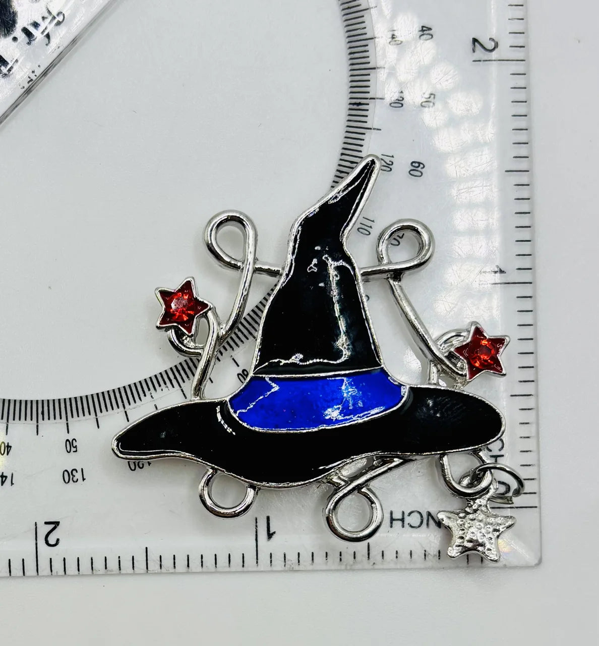 Enamel witch hat with dangling crystals needle minder beside a ruler for scale