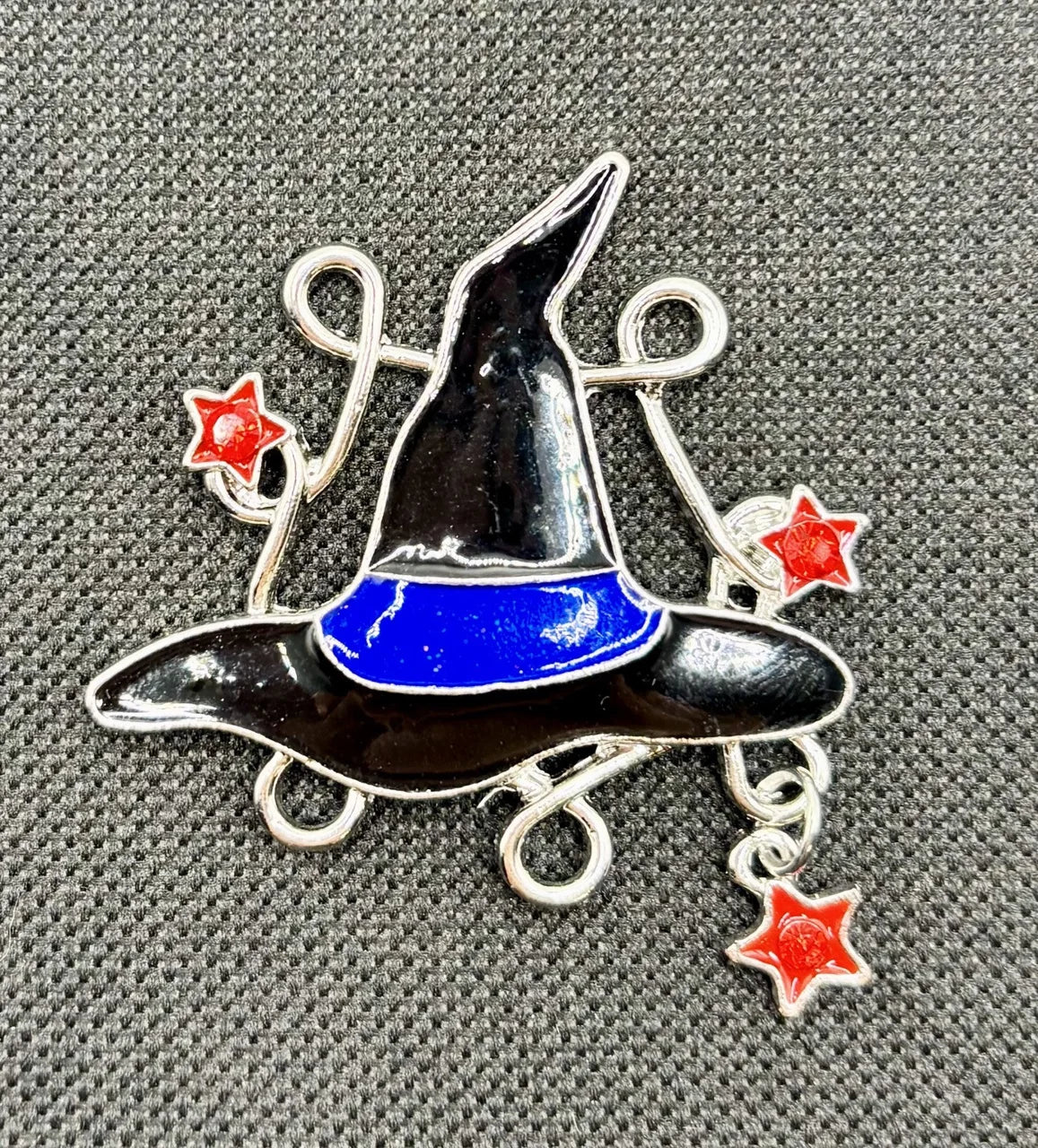 Enamel witch hat with dangling crystals needle minder on dark fabric