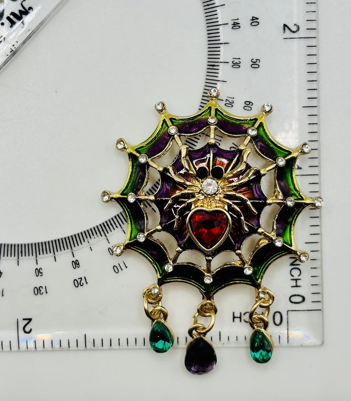 Jeweled spider in web needle minder beside a ruler for scale