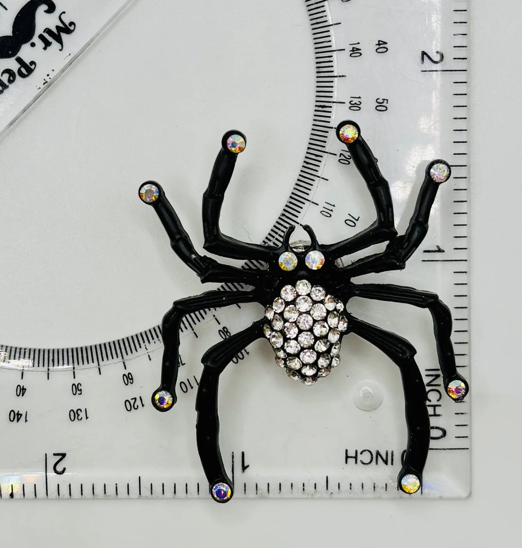 Black spider with crystals needle minder beside a ruler for scale