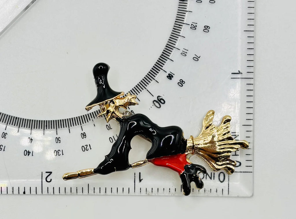 Enamel flying witch needle minder beside a ruler for scale
