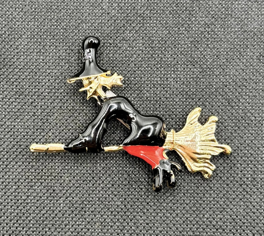 Enamel flying witch needle minder on dark fabric