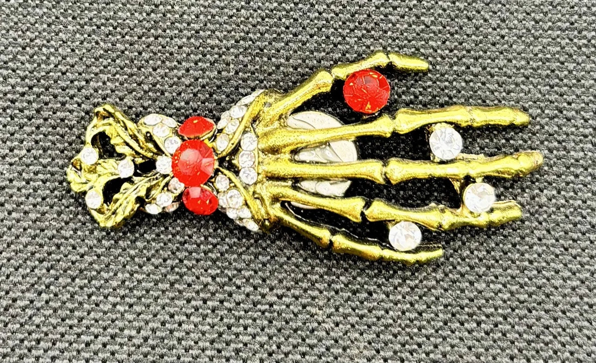 Gold and crystal skeleton hand needle minder on dark fabric