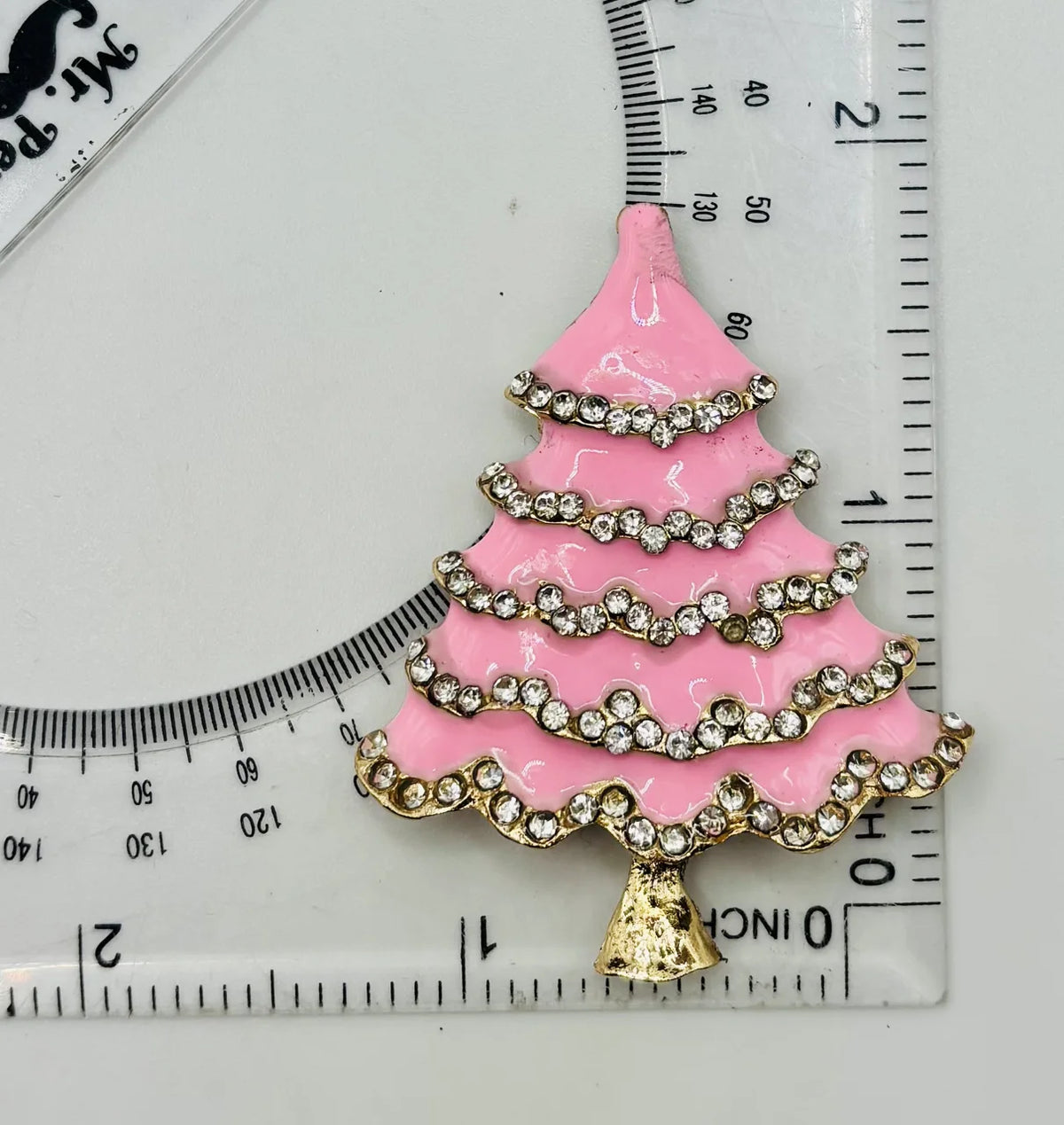 Pink enamel tree with crystals needle minder beside a ruler for scale