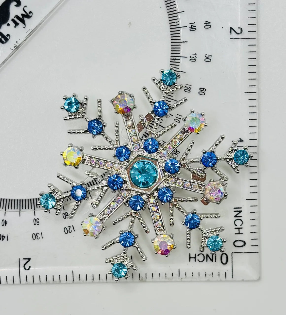 Blue crystal snowflake needle minder beside a ruler for scale