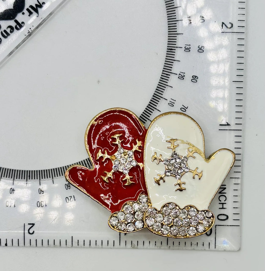 White and red enamel mittens needle minder beside a ruler for scale