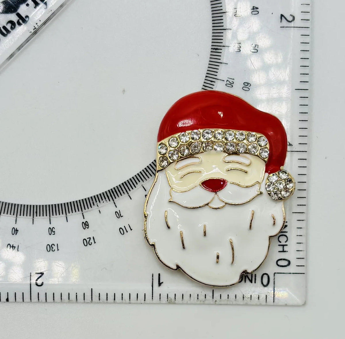 Enamel Santa face needle minder beside a ruler for scale