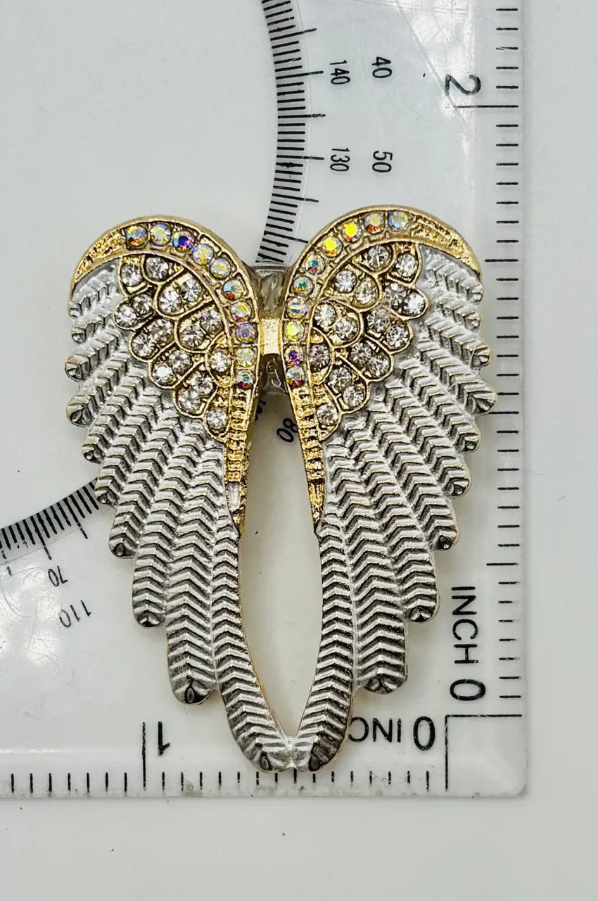 White enamel and crystal angel wings needle minder beside a ruler for scale