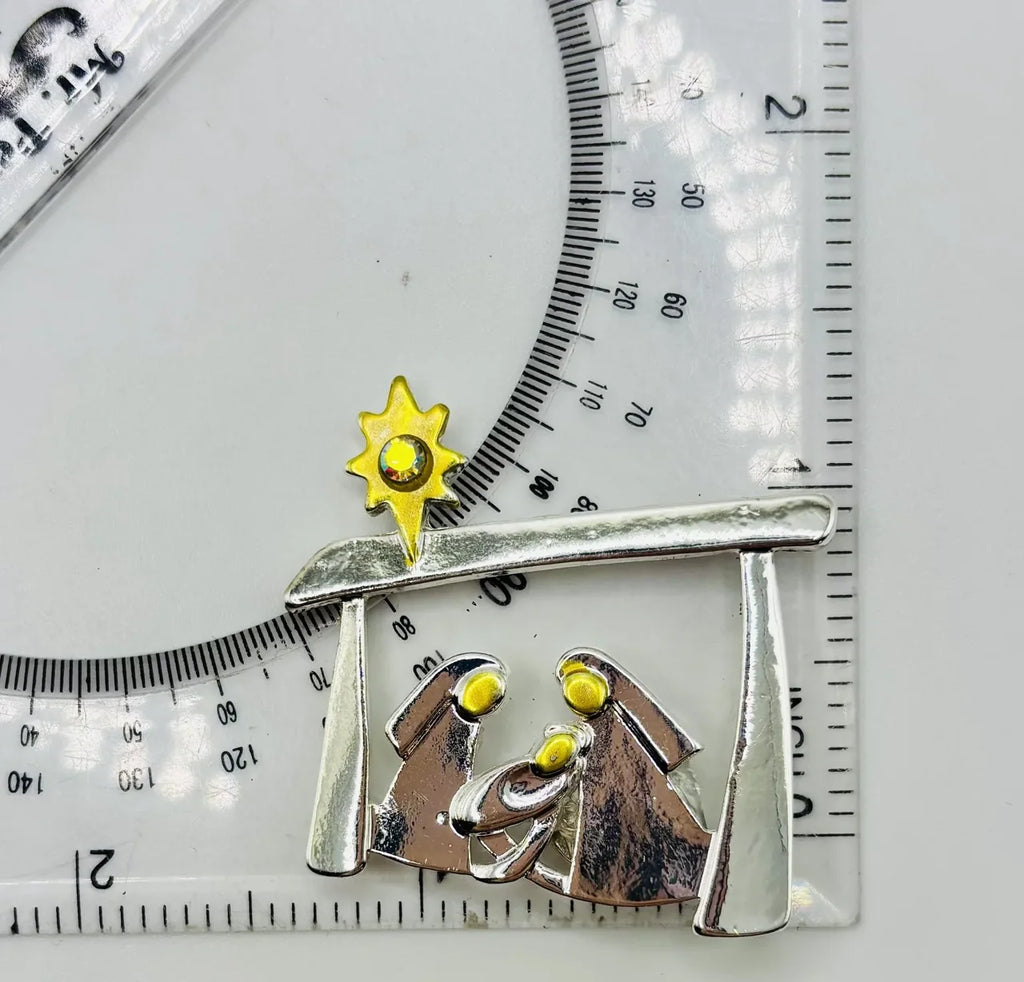 Silver and gold metal Holy Family needle minder beside a ruler for scale