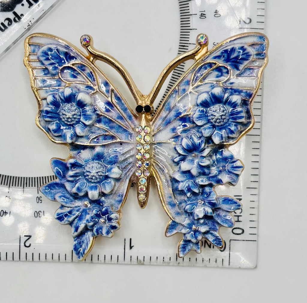 Blue enamel butterfly needle minder beside a ruler for scale