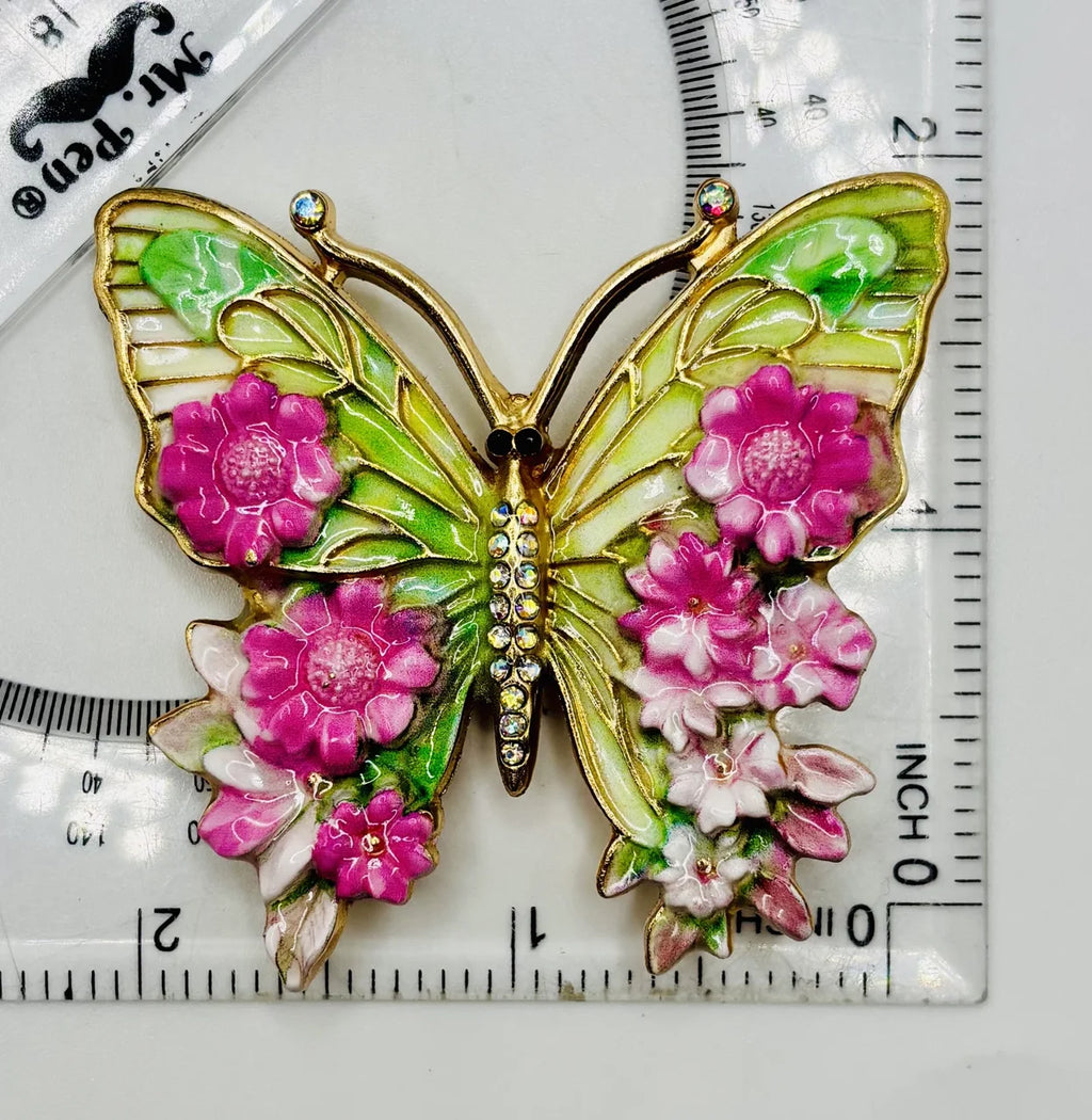 Pink and green enamel butterfly needle minder beside a ruler for scale