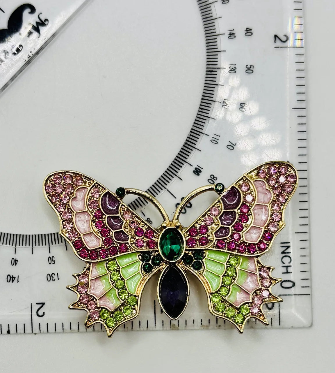 Red white and pink and green enamel crystal butterfly needle minder beside a ruler for scale