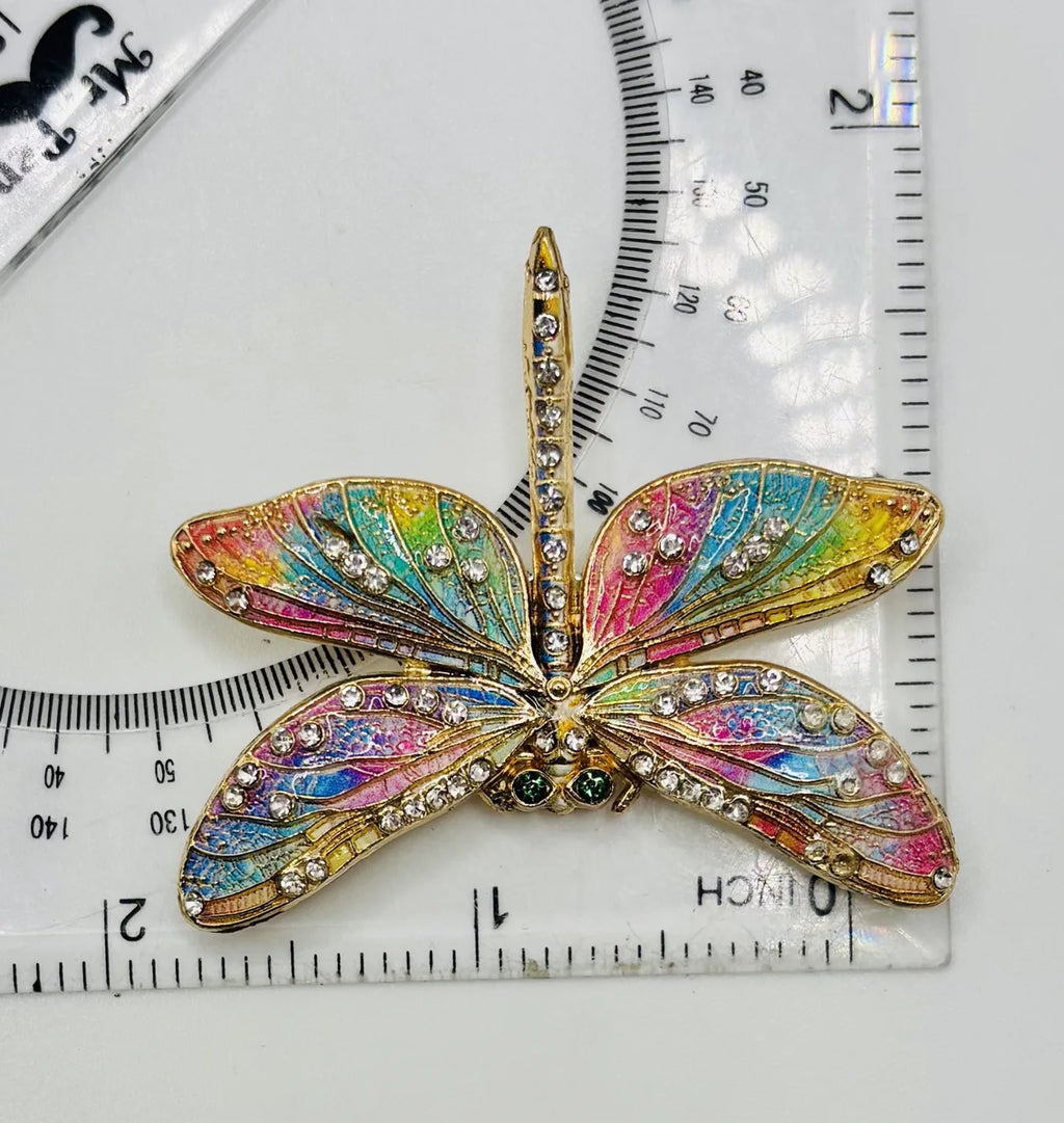 Red white and pastel rainbow enamel crystal dragonfly needle minder beside a ruler for scale