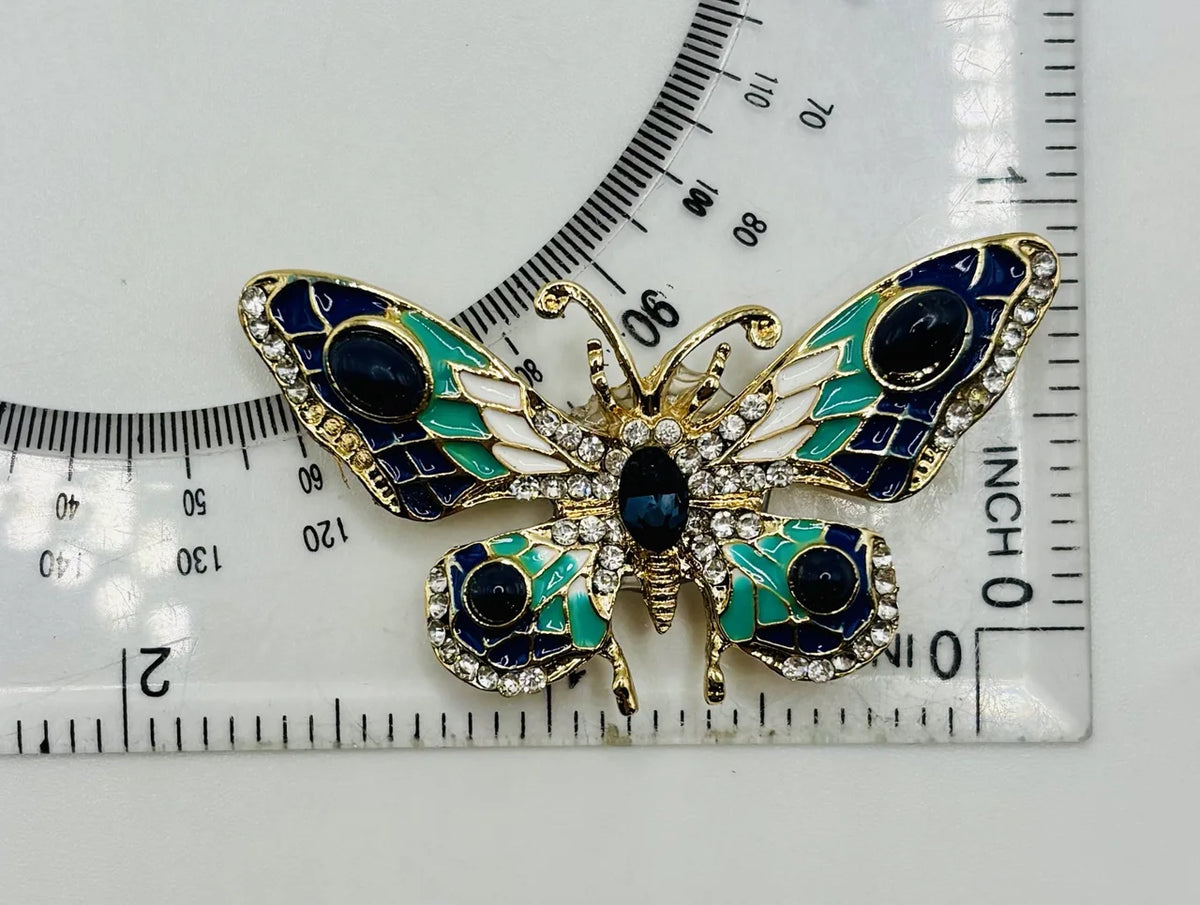 Red white and small blue green and white enamel crystal butterfly needle minder beside a ruler for scale