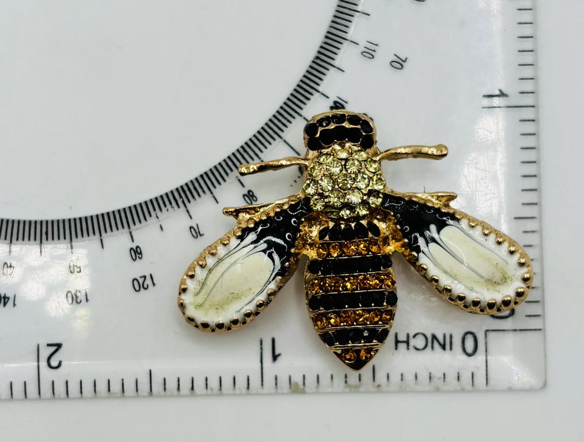 Little enamel and crystal bee needle minder beside a ruler for scale