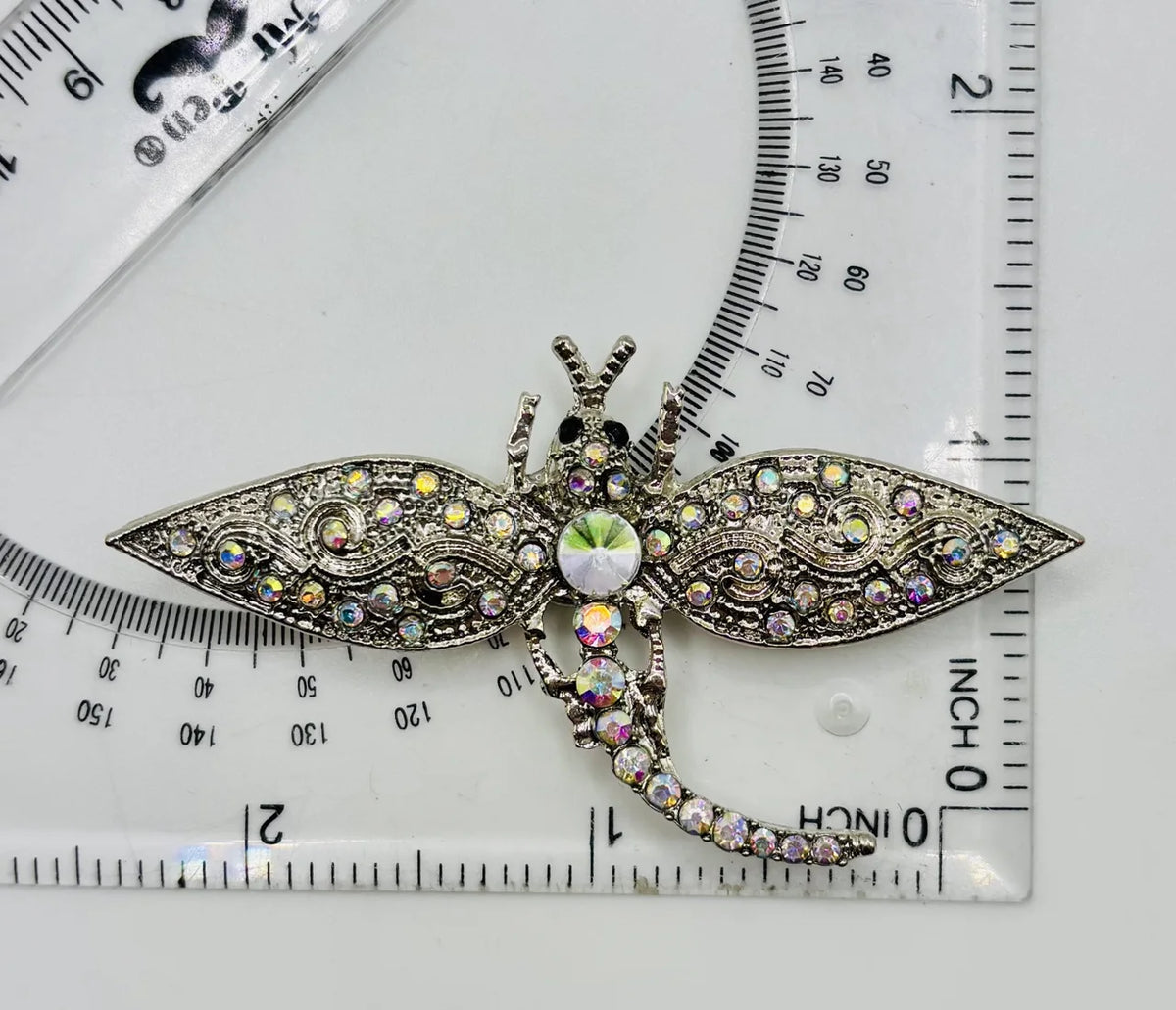 Silver and crystal dragonfly needle minder beside a ruler for scale