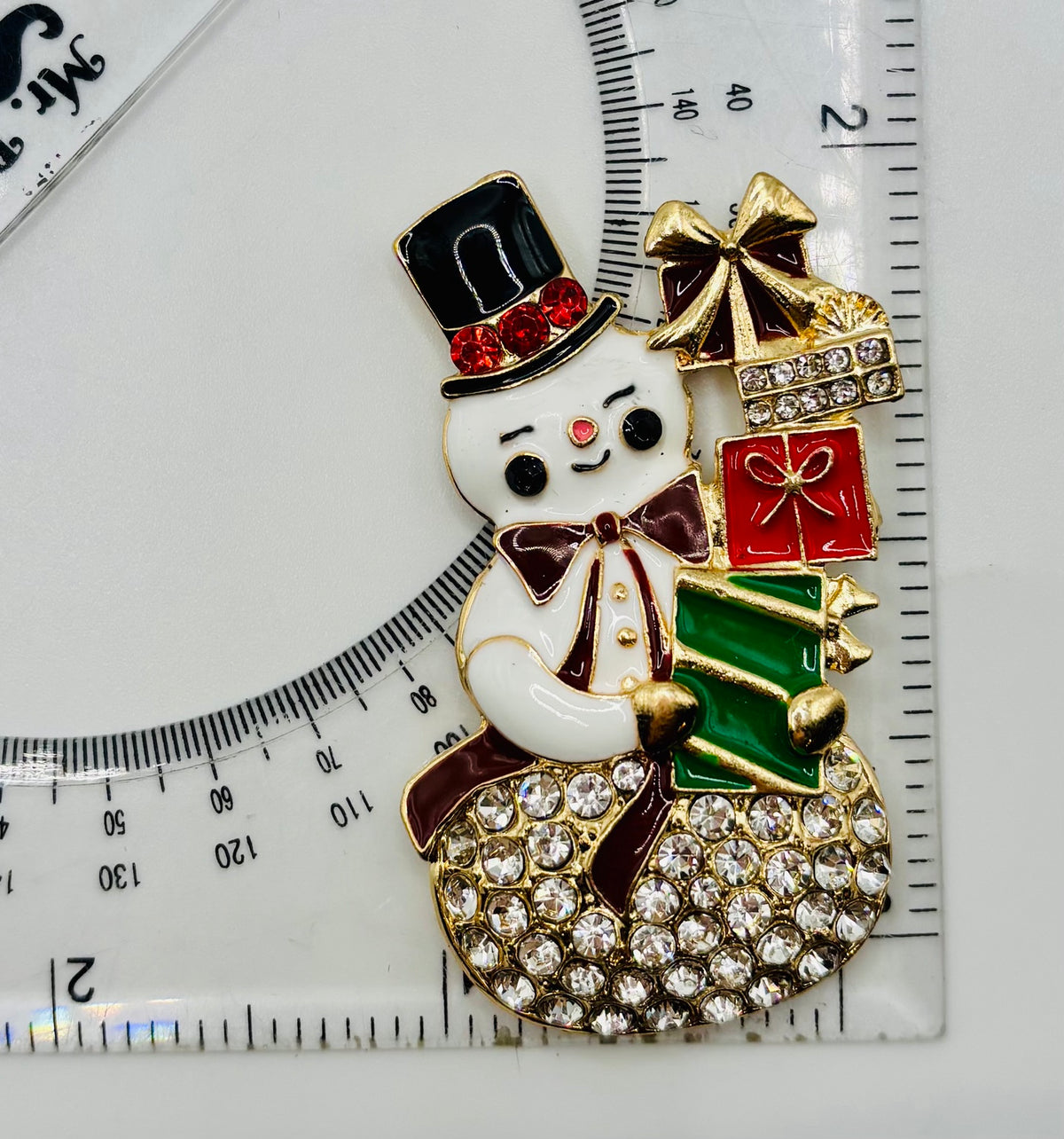 Crystal snowman with gifts needle minder beside a ruler for scale