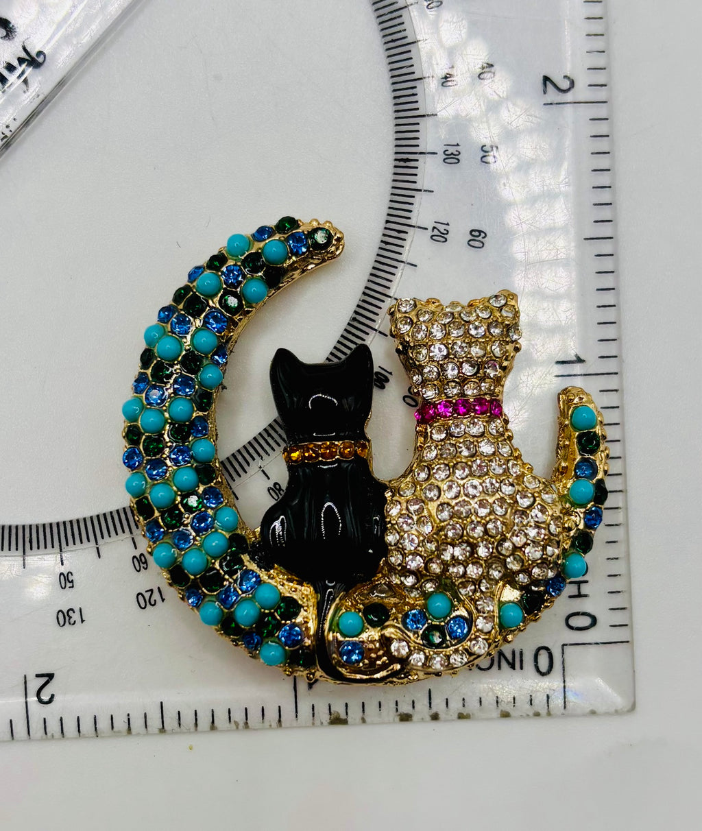 Black and crystal cats on turquoise moon needle minder beside a ruler for scale