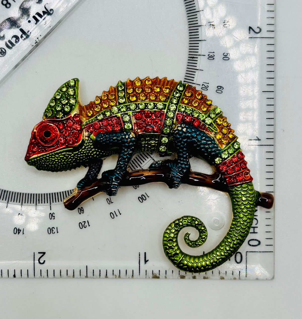Colorful crystal chameleon needle minder beside ruler for scale