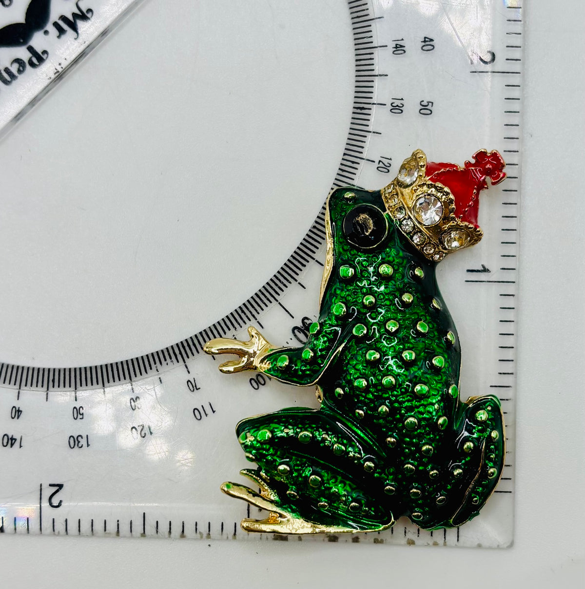 Dark green frog king needle minder beside ruler for scale