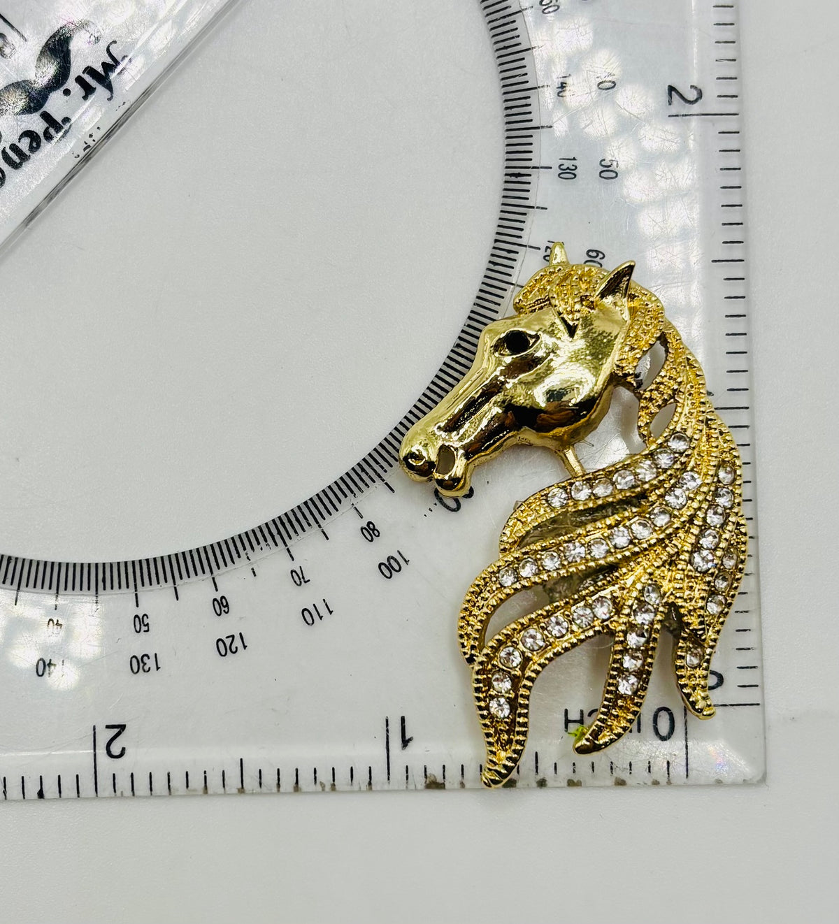 Gold and crystal horse head needle minder beside a ruler for scale