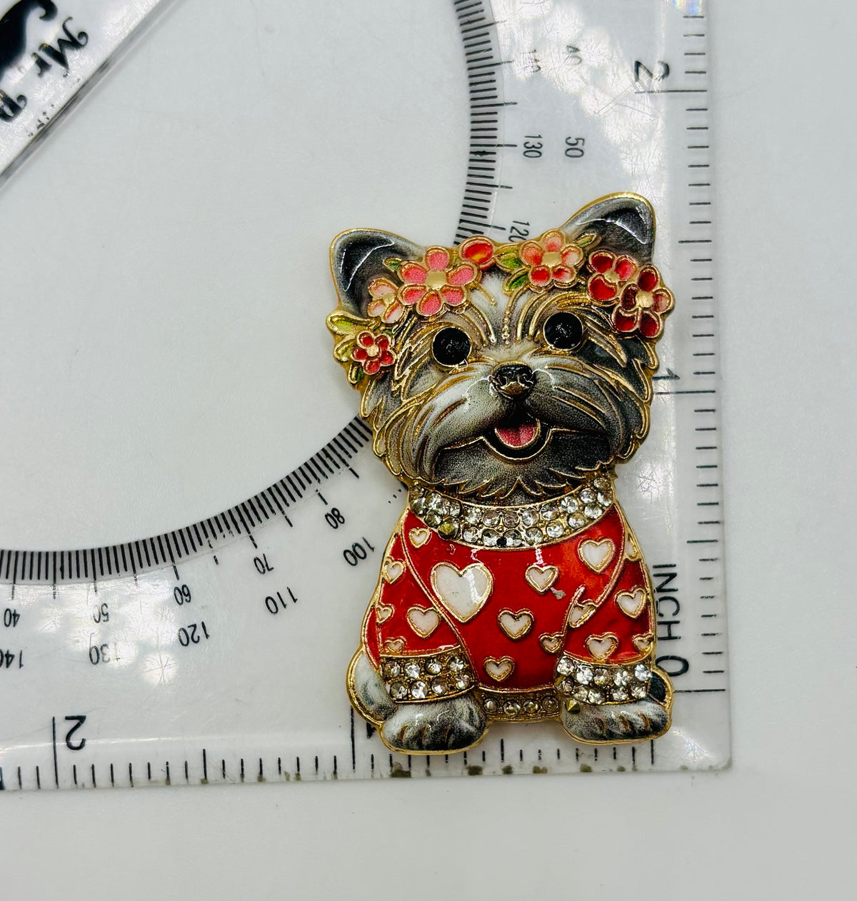 Gray dog in red heart sweater needle minder beside a ruler for scale