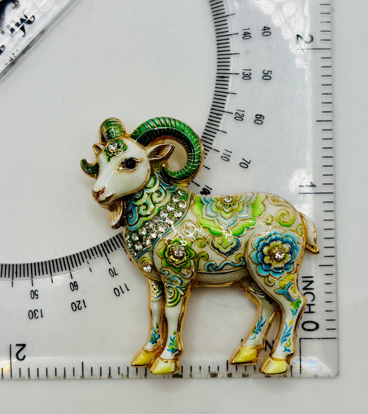 Green floral goat needle minder beside ruler for scale