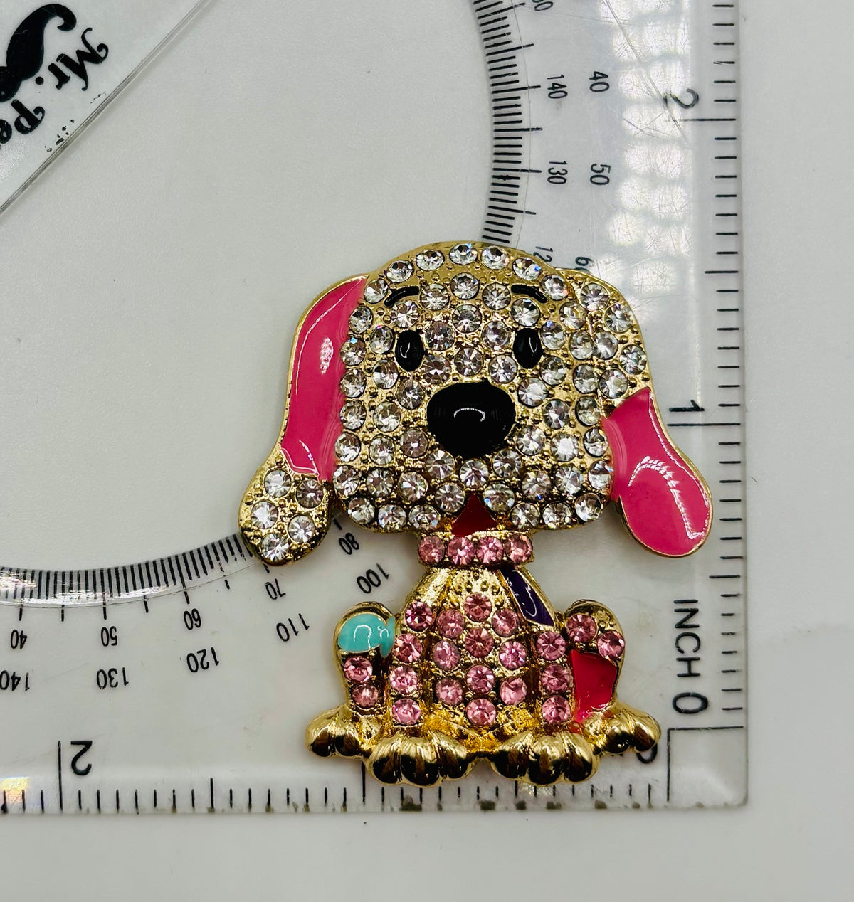 Large pink crystal dog needle minder beside a ruler for scale