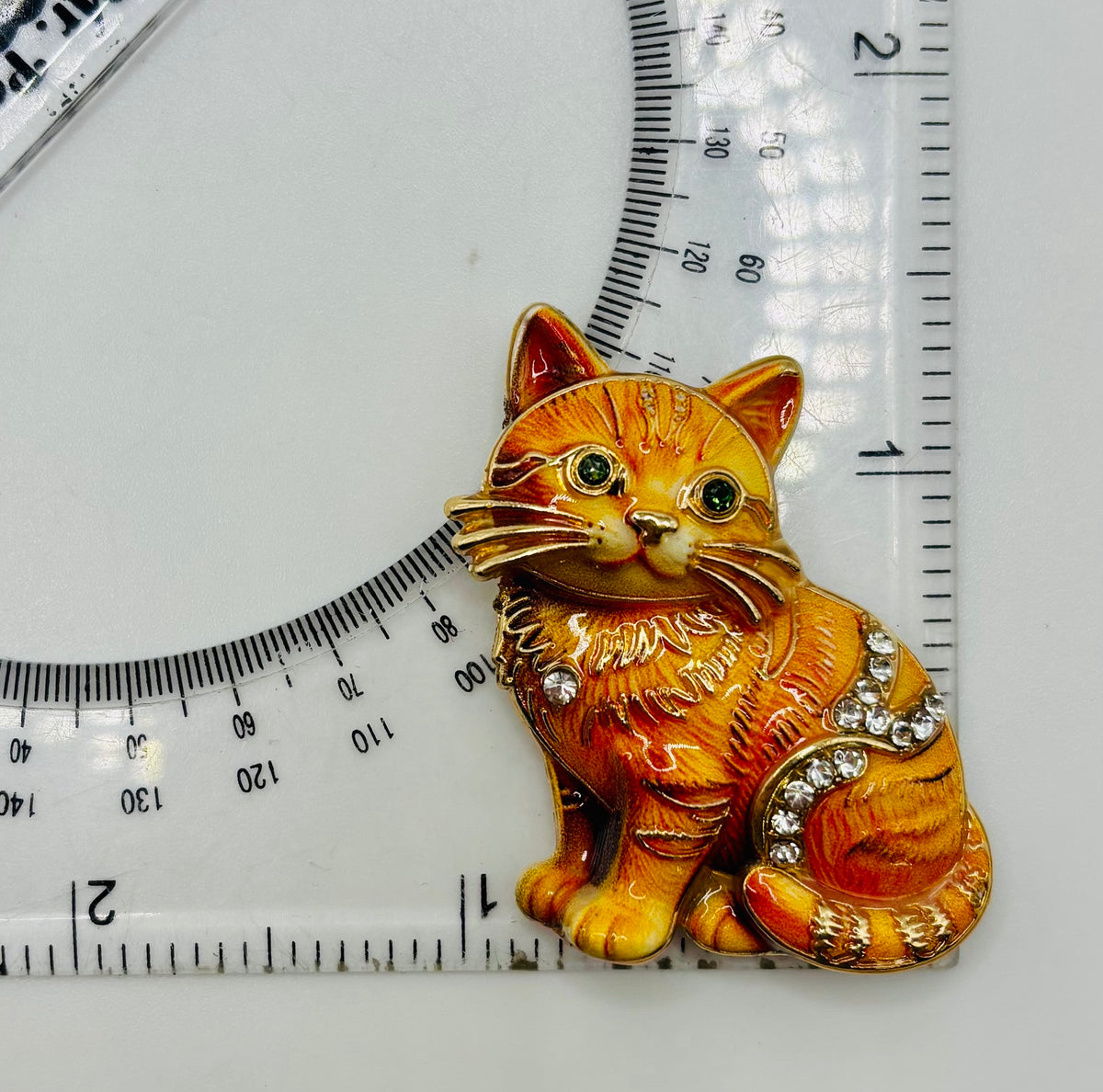 Orange tabby cat kitty needle minder beside a ruler for scale