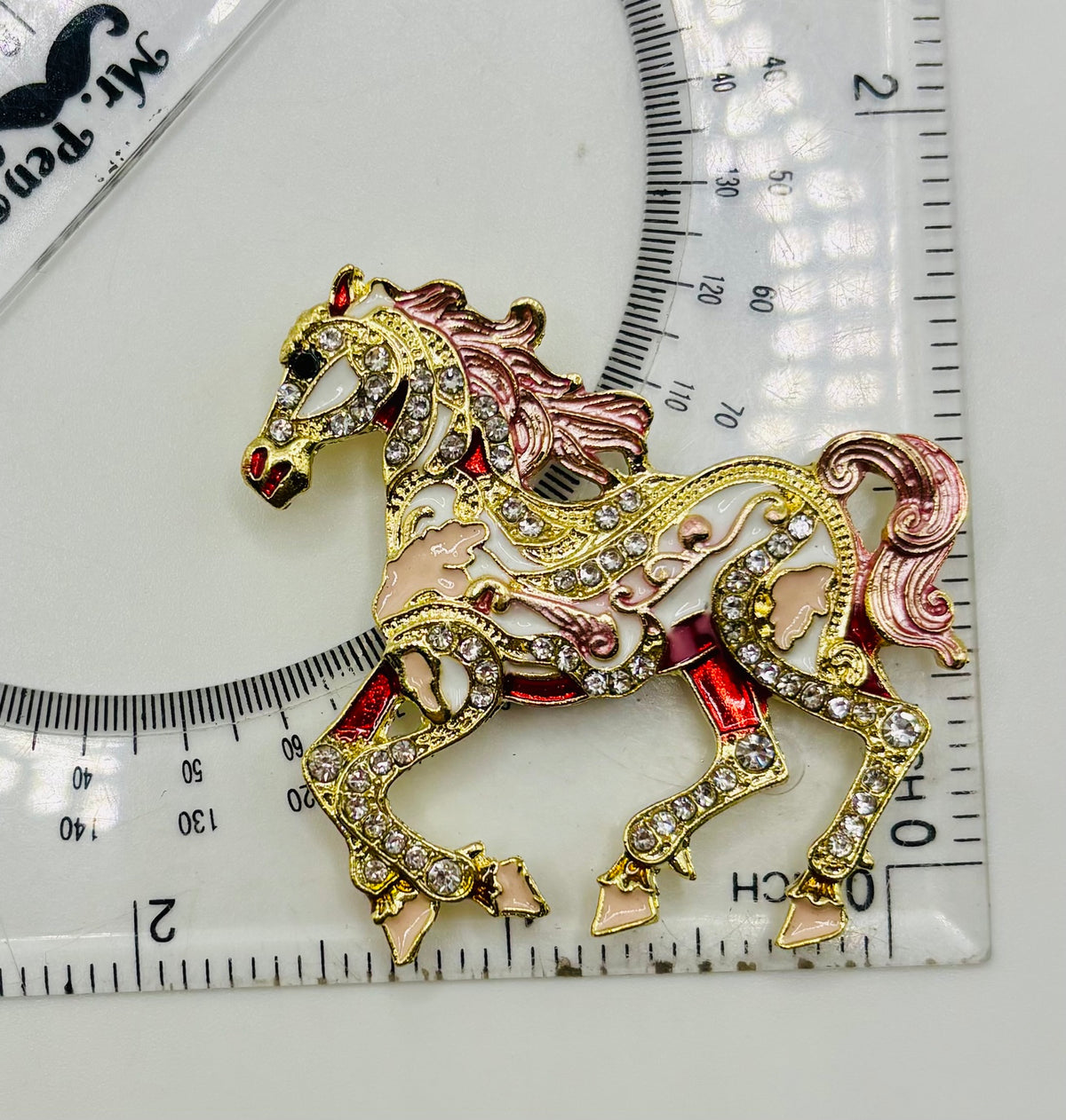 Pink scroll horse needle minder beside a ruler for scale
